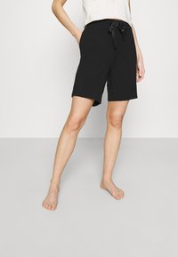 Shorts noirs en tissu doux avec une taille élastique et un détail de ruban noué. Comprend des poches latérales et une coupe décontractée.