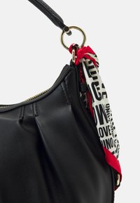 Svart läderhandväska med en böjd form, guldfärgade detaljer, och en mönstrad tygscarf i vitt och rött knuten vid handtaget.