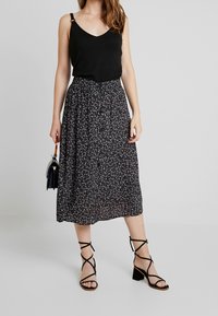 Černý žebrovaný top bez rukávů, květinová midi sukně v černé, červené a bílé barvě s detailním knoflíkem, doplněná černými sandály na podpatku se stahováním.