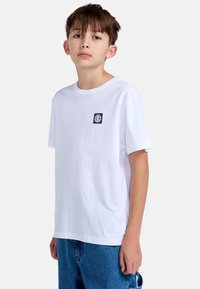 Witte katoenen t-shirt met een ronde hals en korte mouwen, met een klein marineblauw logo op de linkerborst, gecombineerd met blauwe denim broek.