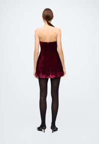 Burgundy velvet strapless dress with a fitted bodice and flared skirt, paired with black sheer tights and black heeled shoes.