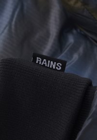 Black knit fabric with a label that reads "RAINS," placed against a light blue interior lining with a textured surface.