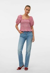 Top a maniche puff in gingham rosso e bianco con orlo arricciato, abbinato a jeans in denim chiaro e décolleté rossi con dettaglio a fiocco.