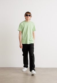Light green cotton t-shirt, black relaxed-fit pants, white sneakers, and black sunglasses. Simple design, no visible patterns or logos.