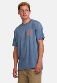 Camiseta de algodón azul con mangas cortas y escote redondo. Presenta una impresión gráfica colorida en la parte izquierda del pecho.