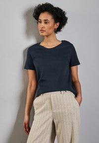 Mörkblå t-shirt med kort ärm i mjukt tyg, kombinerad med ljusbeige randiga byxor med lös passform och sidofickor.