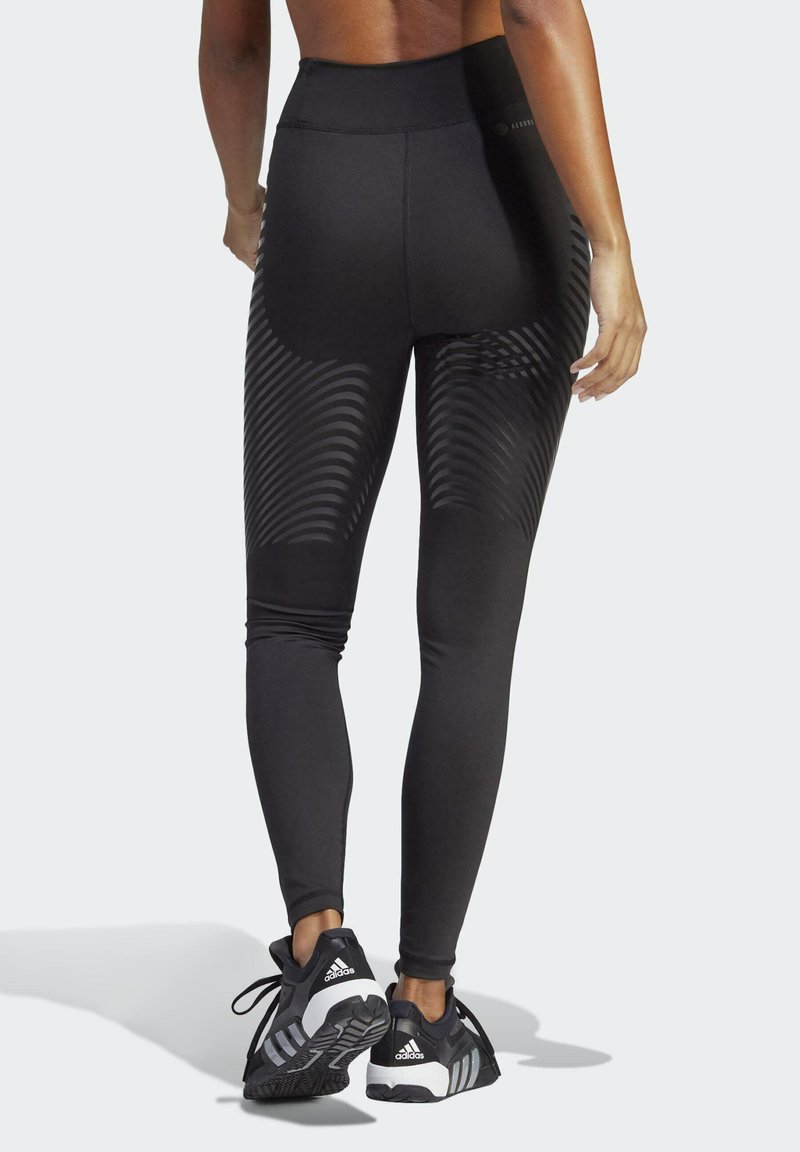 Musta kõrge vöökohaga leggins, millel on tekstuuriga muster, sujuv disain ja sile materjal. Kombineeritud mustade ja valgete spordikingadega.
