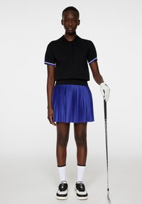 Svart texturerad polo med blå och vita detaljer, i kombination med en veckad blå kjol. Vita strumpor och svarta sneakers fulländar outfiten.