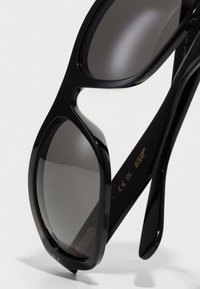 Ochelari de soare negri cu finisaj lucios, lentile ovale supradimensionate și brațe negre elegante. Lentilele cu nuanță gri oferă protecție UV.