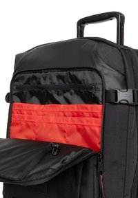 Black wheeled backpack with a black and red interior, featuring a zippered compartment, adjustable straps, and a sturdy handle.