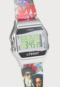 Montre numérique avec un boîtier en acier inoxydable, un écran LCD vert et un bracelet à motifs colorés arborant des graphismes artistiques.