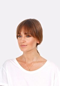 T-shirt bianco, collana d'oro con un pendente circolare, pelle liscia, capelli alla spalle con frangia, trucco naturale, sfondo chiaro.