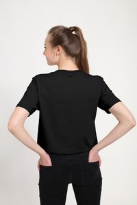 Černé bavlněné tričko s krátkými rukávy, kulatým výstřihem a volným střihem, zobrazené zezadu s rukama položenýma na bocích.