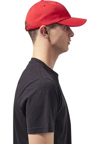 Rode baseballcap van katoen met een gebogen klep, gedragen door een persoon in een zwart t-shirt, zichtbaar in een zijaanzicht.