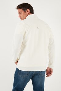 Valge fliiskrae, millel on pikkade varrukatega, peene logosümboliga seljal, koos siniste denimitehingatega.