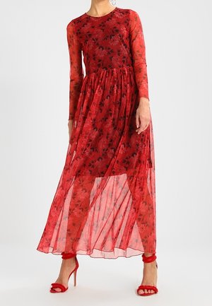 Red maxi dress with long sheer sleeves, floral pattern, cinched waist, and flowing skirt. Paired with red high-heeled sandals.