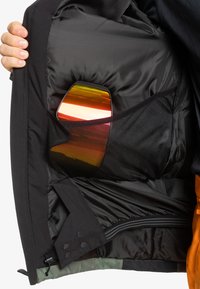 Chaqueta negra con un interior suave y un bolsillo de malla, que muestra gafas de sol coloridas con lentes reflectantes. Incluye un cierre de cremallera y botones a presión.