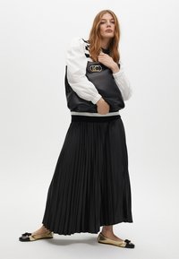 Gonna nera plissettata, blusa a righe bianche e nere con maniche a sbuffo e ballerine con dettagli dorati. La borsa presenta un importante dettaglio con logo.