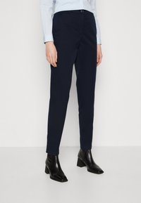 Námornícke slim-fit nohavice vyrobené z bavlny, s plochým predkom, bočnými vreckami a uzatváraním na jeden gombík, skombinované s lesklými čiernymi členkovými čižmami.
