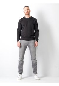Sudadera negra con cuello redondo, mangas largas y puños acanalados. Combinada con jeans gris claro y zapatillas blancas. Diseño simple, sin patrones.