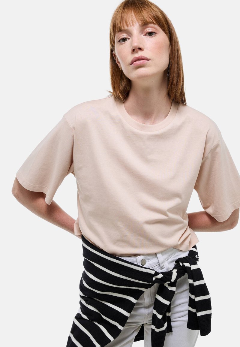 T-shirt rose clair à manches courtes avec un col rond, associé à un pull à rayures noir et blanc noué autour de la taille.