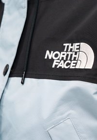 Ελαφρώς μπλε και μαύρο μπουφάν από συνθετικό ύφασμα, με κεντημένο λογότυπο και μπροστινή τσέπη, με κλείσιμο φερμουάρ και κουμπιά.