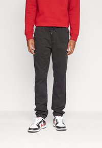 Mörkgrå joggerbyxor med elastiskt midjeband och dragsko, kombinerat med en röd sweatshirt och vita sneakers med svarta detaljer.