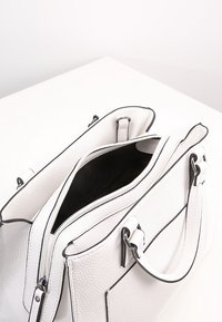 Sac à main en cuir blanc à surface texturée, bordure noire, double poignée et ouverture supérieure laissant voir un intérieur noir.