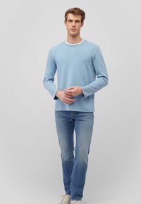 Hellblaues Strickpullover mit langen Ärmeln, Rundhalsausschnitt und gerippter Textur, kombiniert mit hellblauen Jeans und weißen Sneakers.