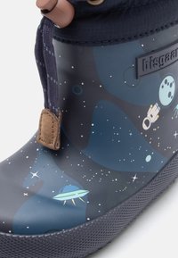 Botte de pluie en caoutchouc noir avec un motif spatial comprenant des étoiles, des planètes et un vaisseau spatial. Semelle texturée et accent en cuir marron près du haut.