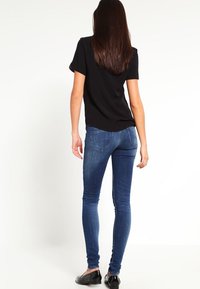 Camiseta negra de manga corta combinada con jeans ajustados de mezclilla azul. Los jeans presentan un diseño clásico de cinco bolsillos y un leve desgaste en los muslos.