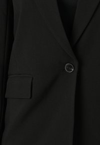 Blazer nero in tessuto morbido, caratterizzato da una chiusura con un solo bottone, rever a lancia e una tasca sul petto con un design minimalista.