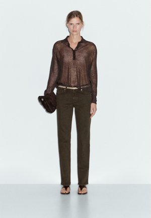 Sheer brown long-sleeve shirt with buttons and a collar, paired with olive green trousers, accented by a studded belt and black clutch.