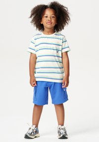 Gestreept t-shirt met korte mouwen en een borstzak, blauwe cargoshorts en sneakers. Het shirt heeft groene en blauwe horizontale strepen.