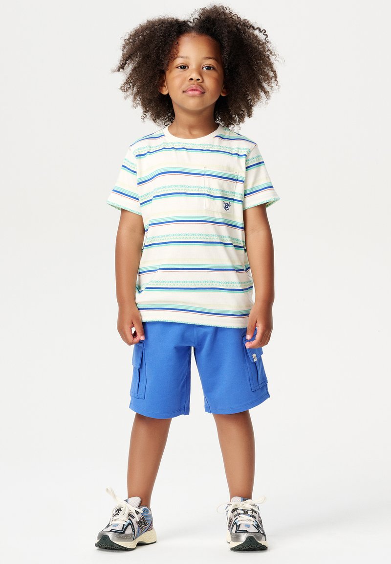 Gestreept t-shirt met korte mouwen en een borstzak, blauwe cargoshorts en sneakers. Het shirt heeft groene en blauwe horizontale strepen.