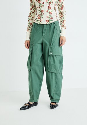 Groene cargobroek van katoen, met een relaxte pasvorm, grote zijzakken en een knoopsluiting. Gepaard met een geribbelde bloemen top en zwarte flats.