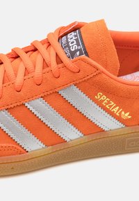 Orange Adidas Spezial-sneaker med mockaliknande yta, tre silverränder, gummisula och märkning på tungan och sidodetaljer.
