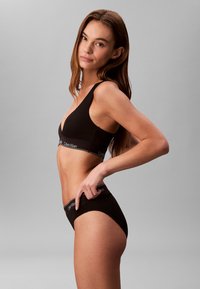 Czarny seamless bralet z szerokimi ramiączkami, z logo Calvin Klein w pasie; dopasowane czarne majtki z wysokim stanem, gładka tekstura, minimalny design.