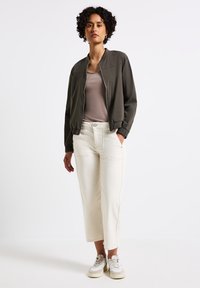 Olivgrön bomberjacka med elastiska manschetter, parat med ljusbeige cropped byxor. Modellen bär vita sneakers med strukturerade detaljer.