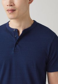Chemise henley bleu marine en tissu doux, avec un col rond, trois boutons et des manches courtes au toucher lisse.