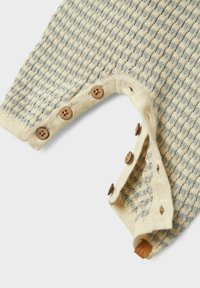 Gros plan sur un tissu en tricot texturé beige et gris avec une rangée de cinq boutons en bois et les boutonnières correspondantes sur le bord.