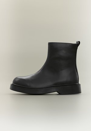 Black leather ankle boot with round toe, pull tab at heel, and thick sole against light neutral background.