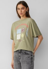 Licht olijfgroene katoenen T-shirt met korte mouwen. Grafiek aan de voorkant bevat tekst en zon, golf en abstracte ontwerpen in meerdere kleuren.