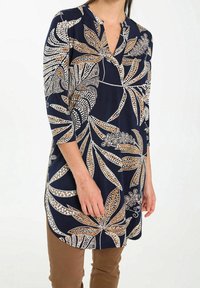 Granatowa tunika z kwiatowym wzorem w bieli i złocie. Wykonana z gładkiego materiału, z mandaryńskim kołnierzem i rękawami o długości trzy czwarte.