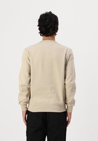 Sudadera beige de manga larga con puños acanalados, con un cuello redondo estándar y un detalle cosido en la parte posterior.