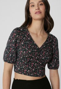 Schwarzes, floral gemustertes, kurzes Oberteil mit kurzen Puffärmeln, V-Ausschnitt und Rüschendetail, verziert mit rosa und weißen Blumenmustern.