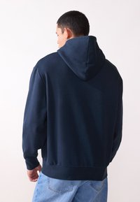 Navy blue hoodie with a spacious hood, ribbed cuffs, and hem, made from a soft, textured fabric. Back view shows a simple design.