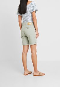 Světlé zelené šortky z bavlny s ohrnutým lemem a zadní kapsou. Nošeny s kostkovanou halenkou a sandály na ploché podrážce.