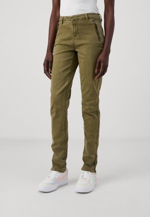 Olivově zelené slim-fit kalhoty se zipovými kapsami, vyrobené z odolné látky. V kombinaci s bílými teniskami s pastelovými akcenty.