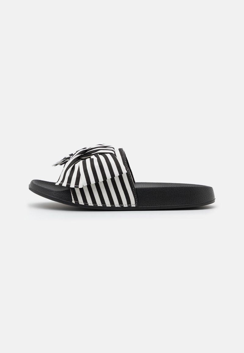 Sandales à enfiler à rayures noires et blanches avec un détail nœud, dotées d'une semelle plate et d'une finition texturée sur la bride et la semelle intérieure.